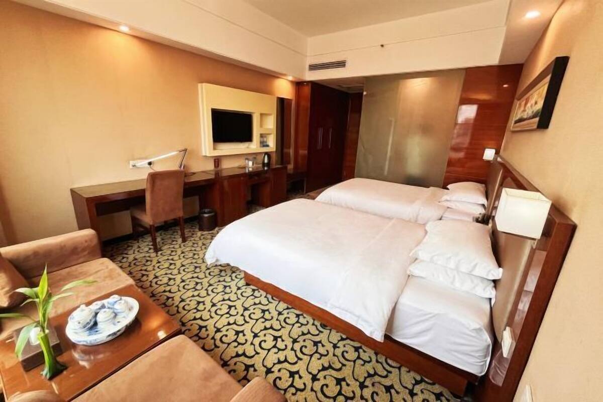 A hotel room with a large bed, a desk with a chair, a television, and a small table with a plant.
