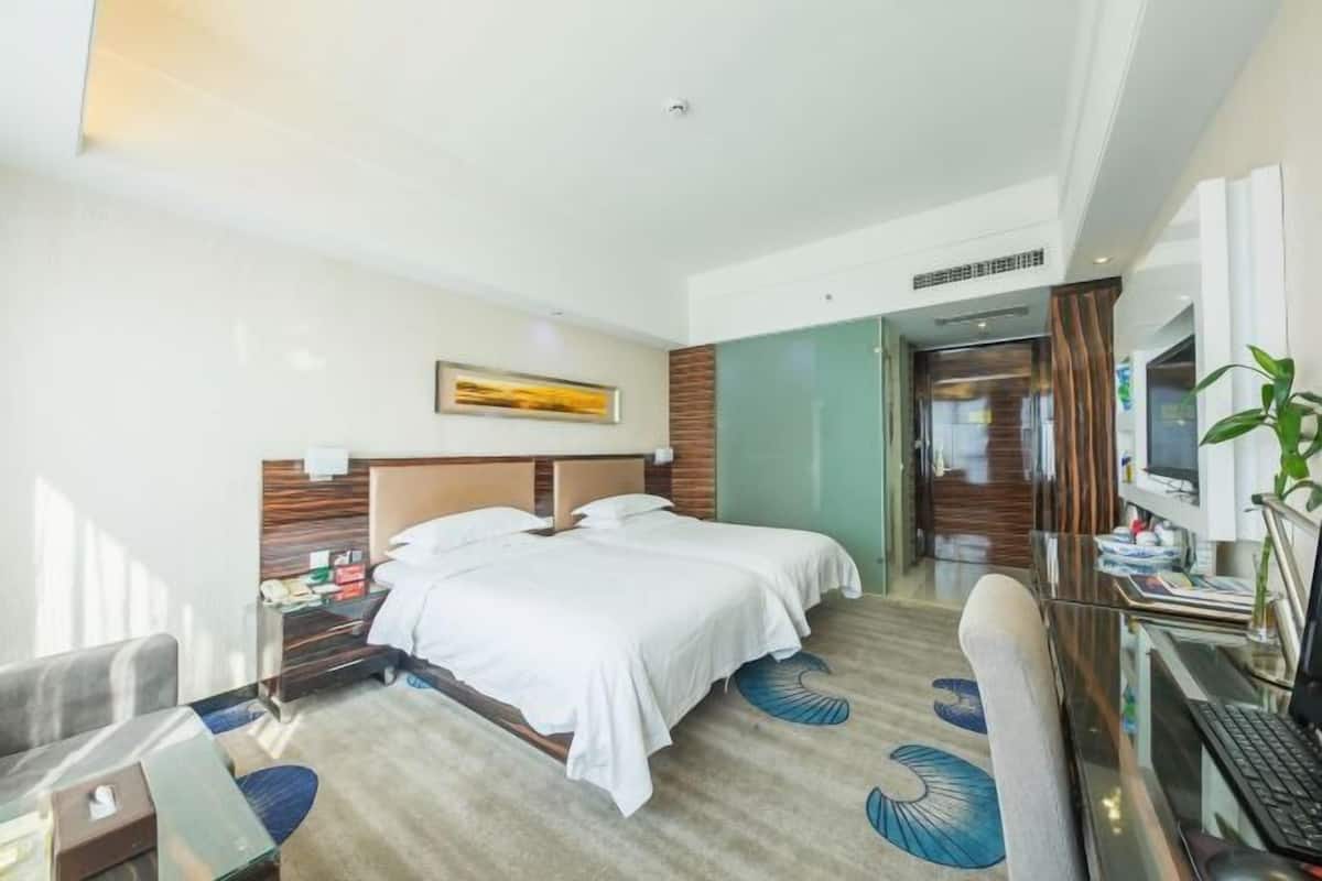 A hotel room with a bed, desk, chair, and a painting on the wall.