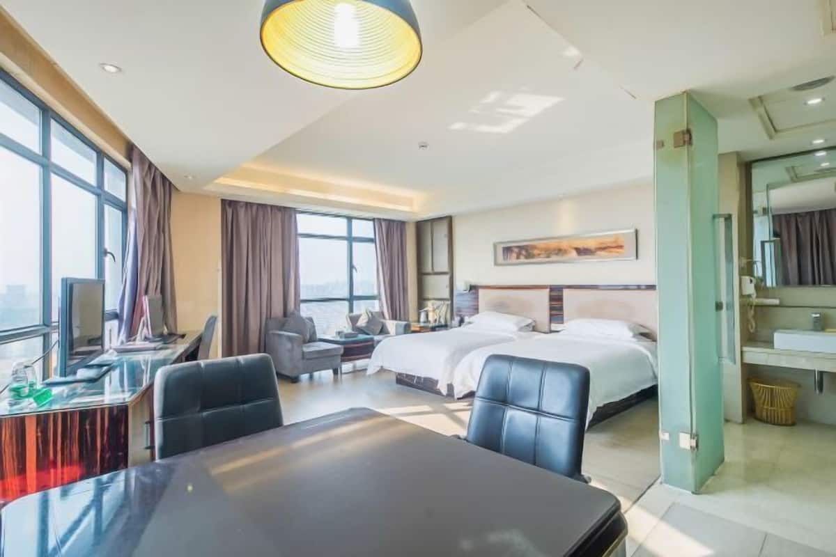 A hotel room with a bed, desk, chair, and a large window.