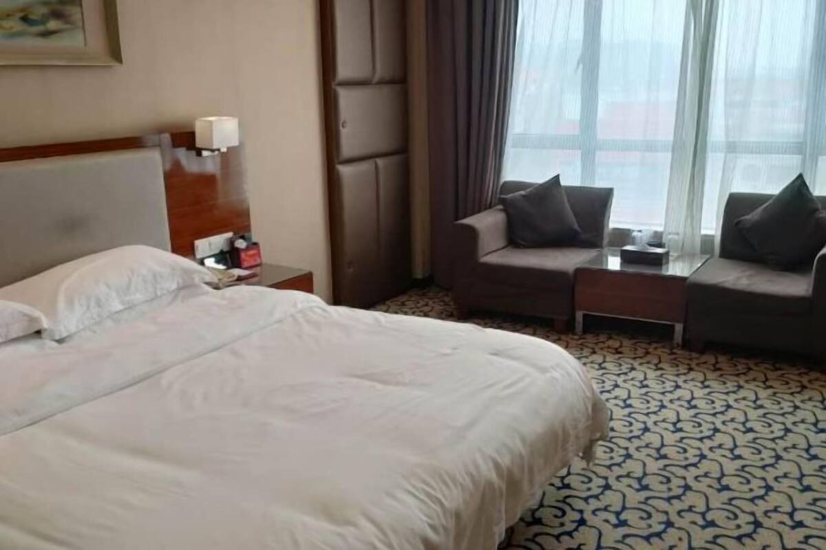 A hotel room with a large bed, a sofa, a small table, and a window with curtains.