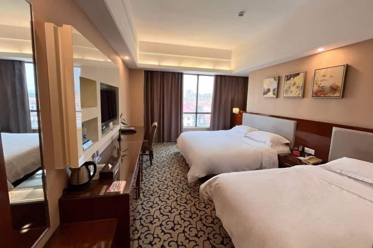 A hotel room with two beds, a TV, a desk with a kettle, and a view of the city.