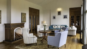 A spacious living room with a fireplace, striped armchairs, a round coffee table, and a blue sofa.