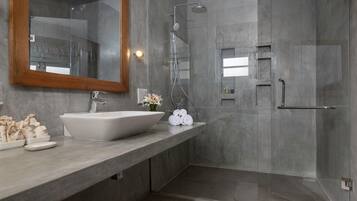 A modern bathroom with a large mirror, a vessel sink, a shower, and a towel rack.