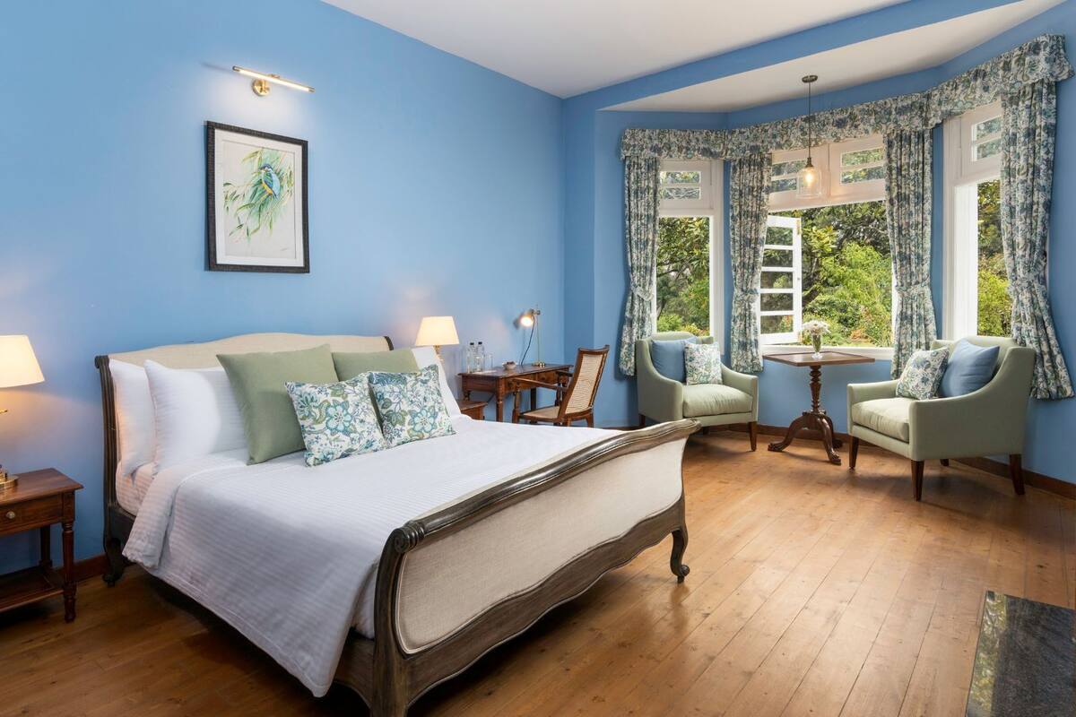 Un dormitorio con una cama grande, dos sillones, una mesita y una ventana con cortinas.