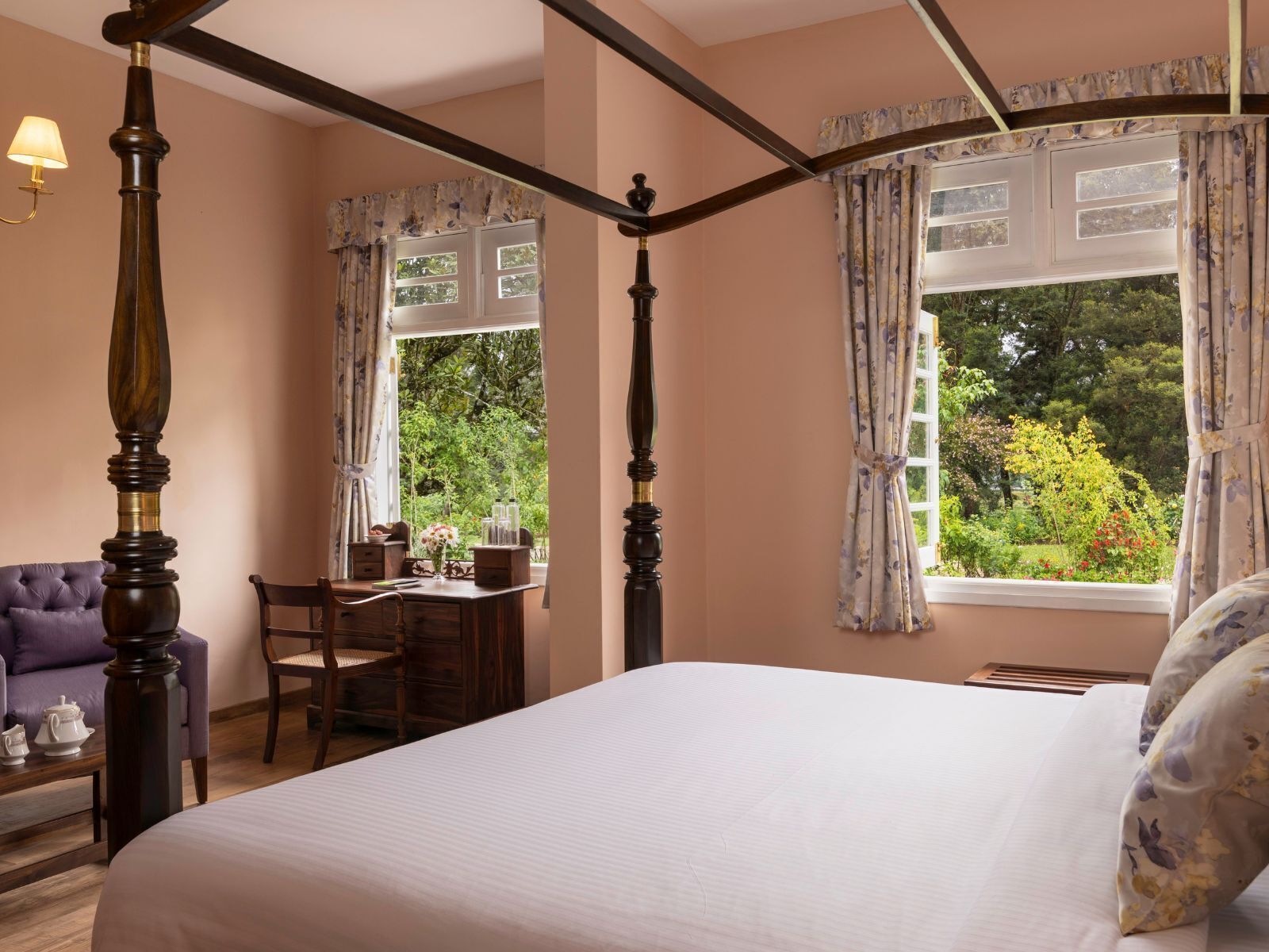 A bedroom with a four-poster bed, a desk with a chair, and a purple armchair.