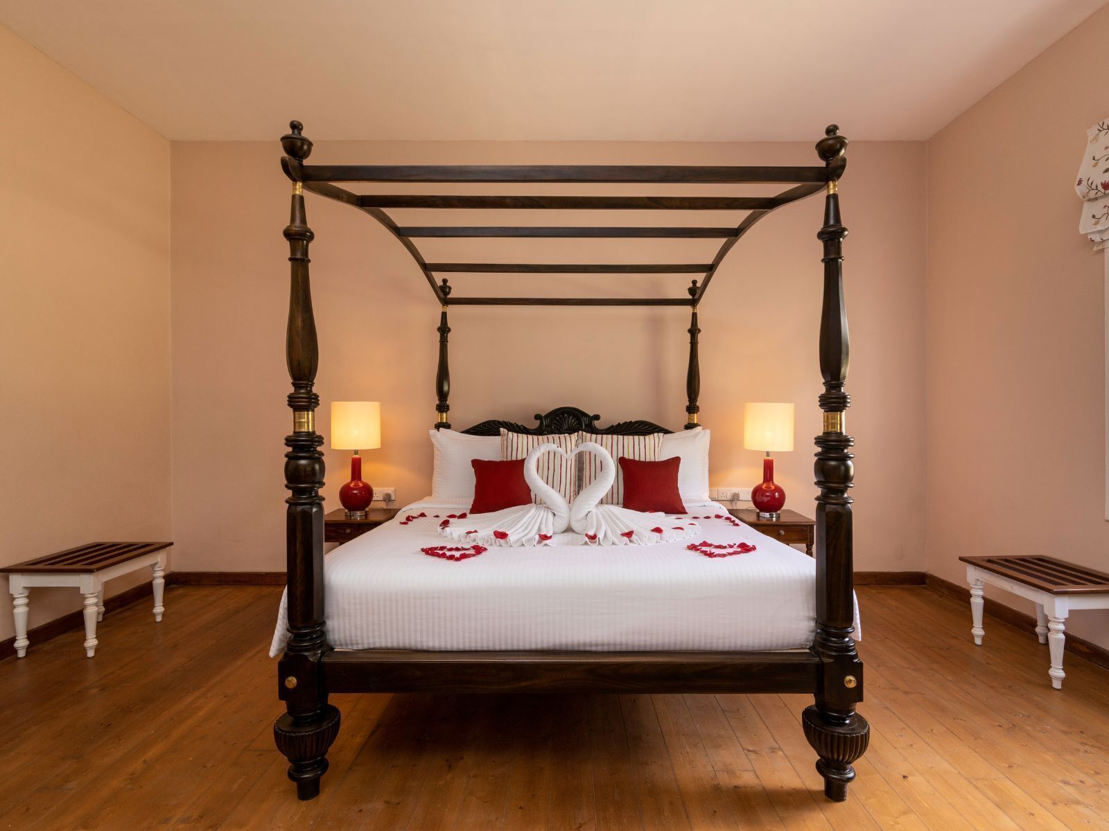 A four-poster bed with a white bedspread and red pillows, flanked by two nightstands with red lamps.