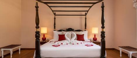 A four-poster bed with a white bedspread and red pillows, flanked by two nightstands with red lamps.