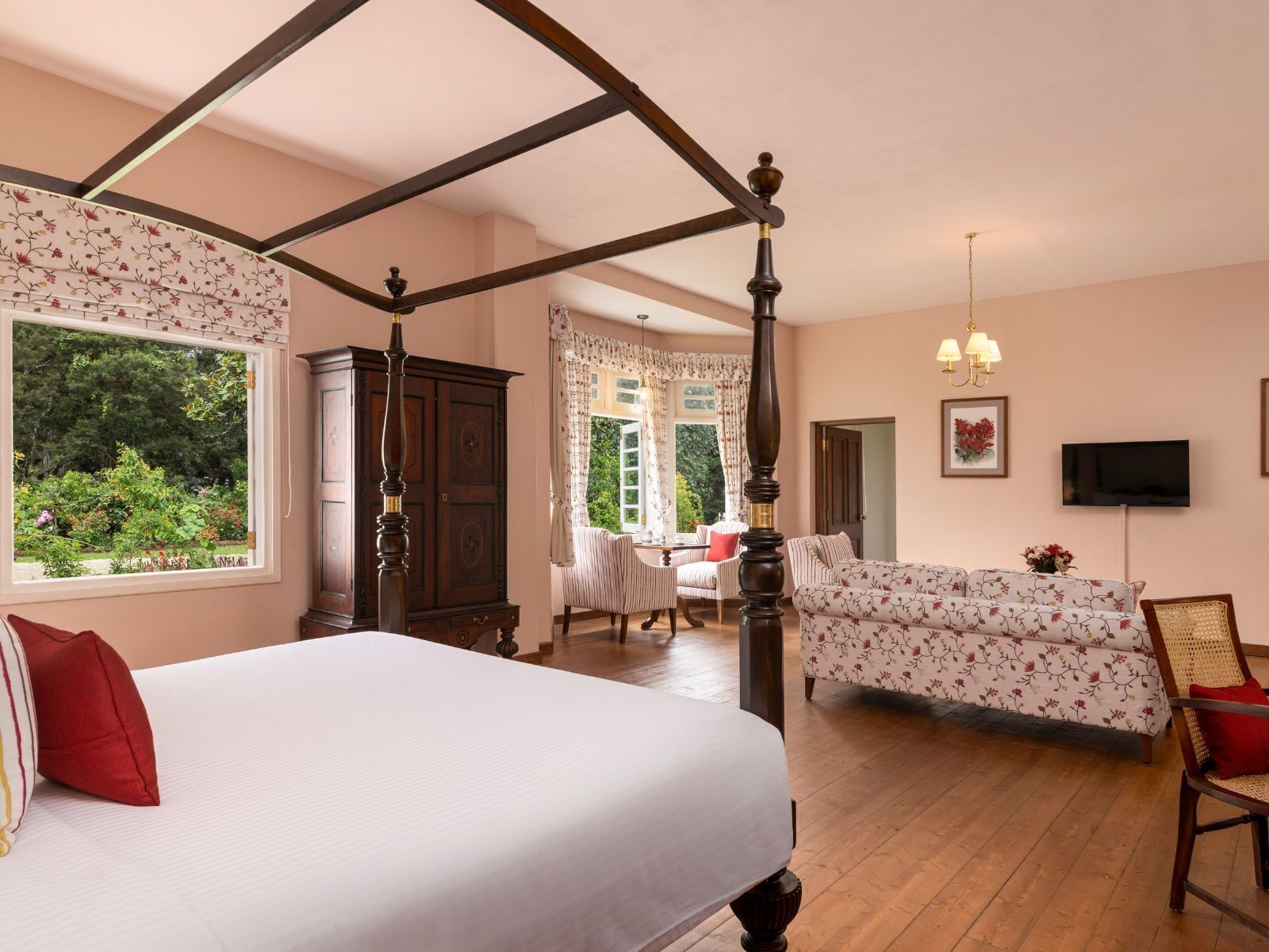 A bedroom with a four-poster bed, a wooden wardrobe, a floral sofa, and a television on the wall.