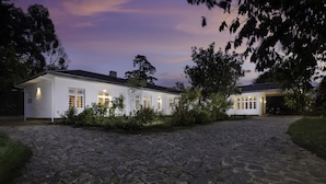 A white house with a stone driveway, surrounded by trees and bushes.