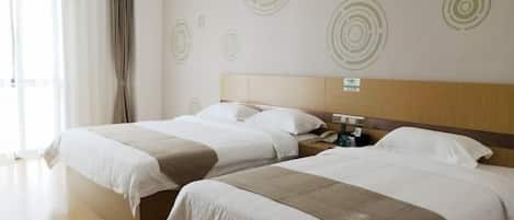 Ein Hotelzimmer mit zwei Betten, einem Holzkopfteil, einem Nachttisch mit Lampe und einem großen Fenster.