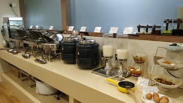 A buffet setup with various food stations, including a coffee station and a fruit bowl.
