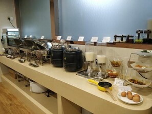 Un buffet avec différents postes de service proposant une variété de plats, notamment un coin café et un présentoir de fruits.