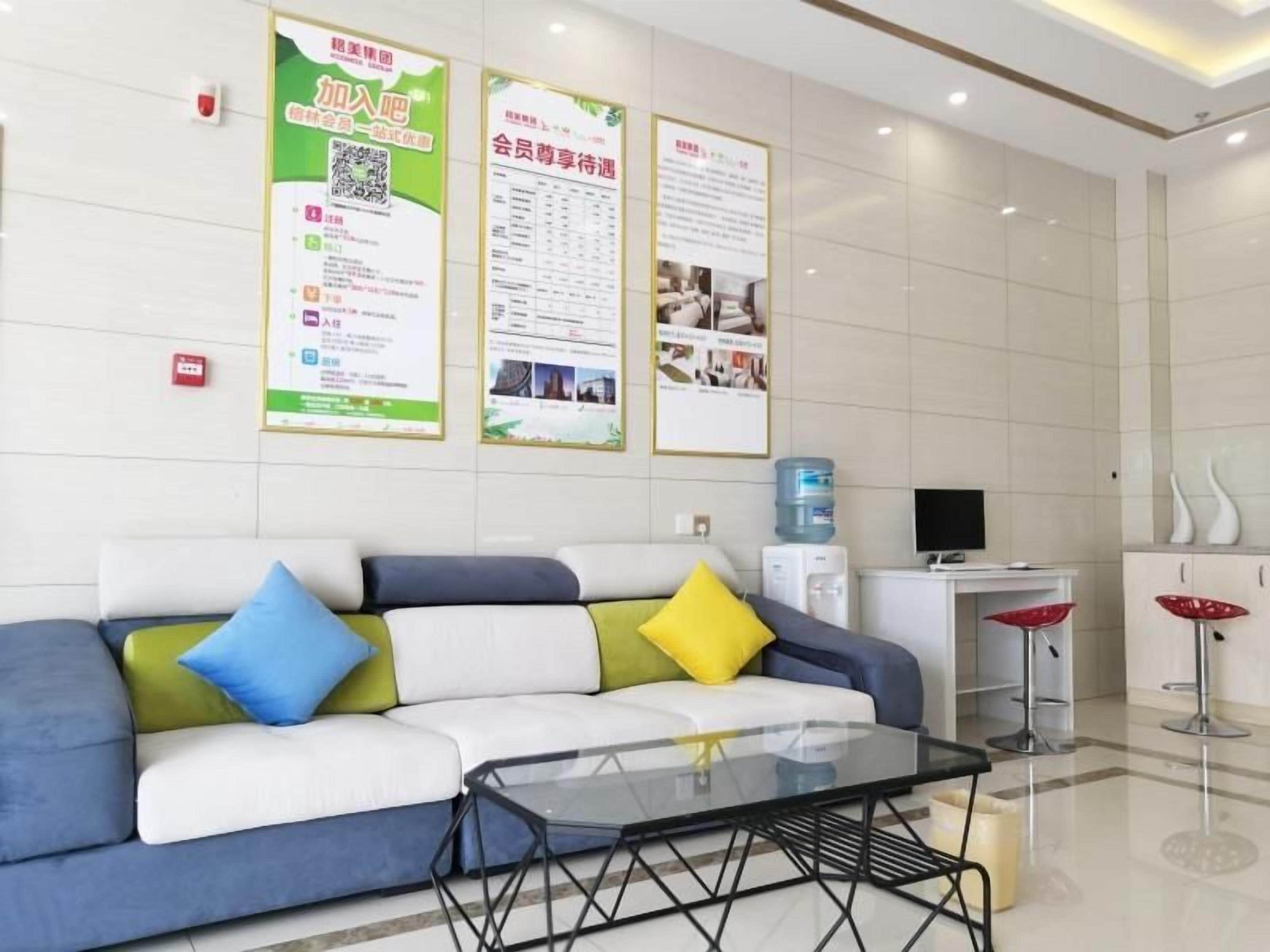 Un área de recepción con un sofá, una mesa de vidrio, un dispensador de agua y carteles informativos en la pared.