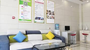 Un área de recepción con un sofá, una mesa de vidrio, un dispensador de agua y carteles informativos en la pared.
