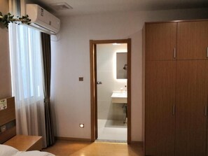 Une chambre d’hôtel comprenant un lit, une armoire en bois, une salle de bain avec un miroir et un appareil de climatisation.