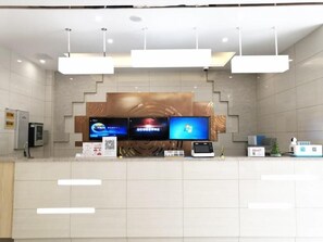 Un espace d’accueil moderne comprenant un comptoir, trois écrans, un kiosque numérique et un mur décoratif.