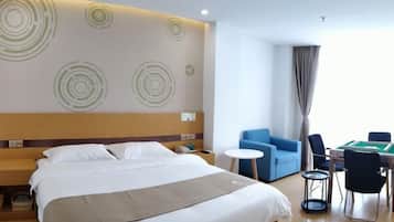 A hotel room with a large bed, a headboard with circular patterns, a small round table, and a blue armchair.