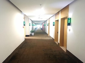 Un couloir d’hôtel avec des revêtements de sol en moquette, des portes sur le côté droit et des panneaux verts indiquant les sorties sur les murs.
