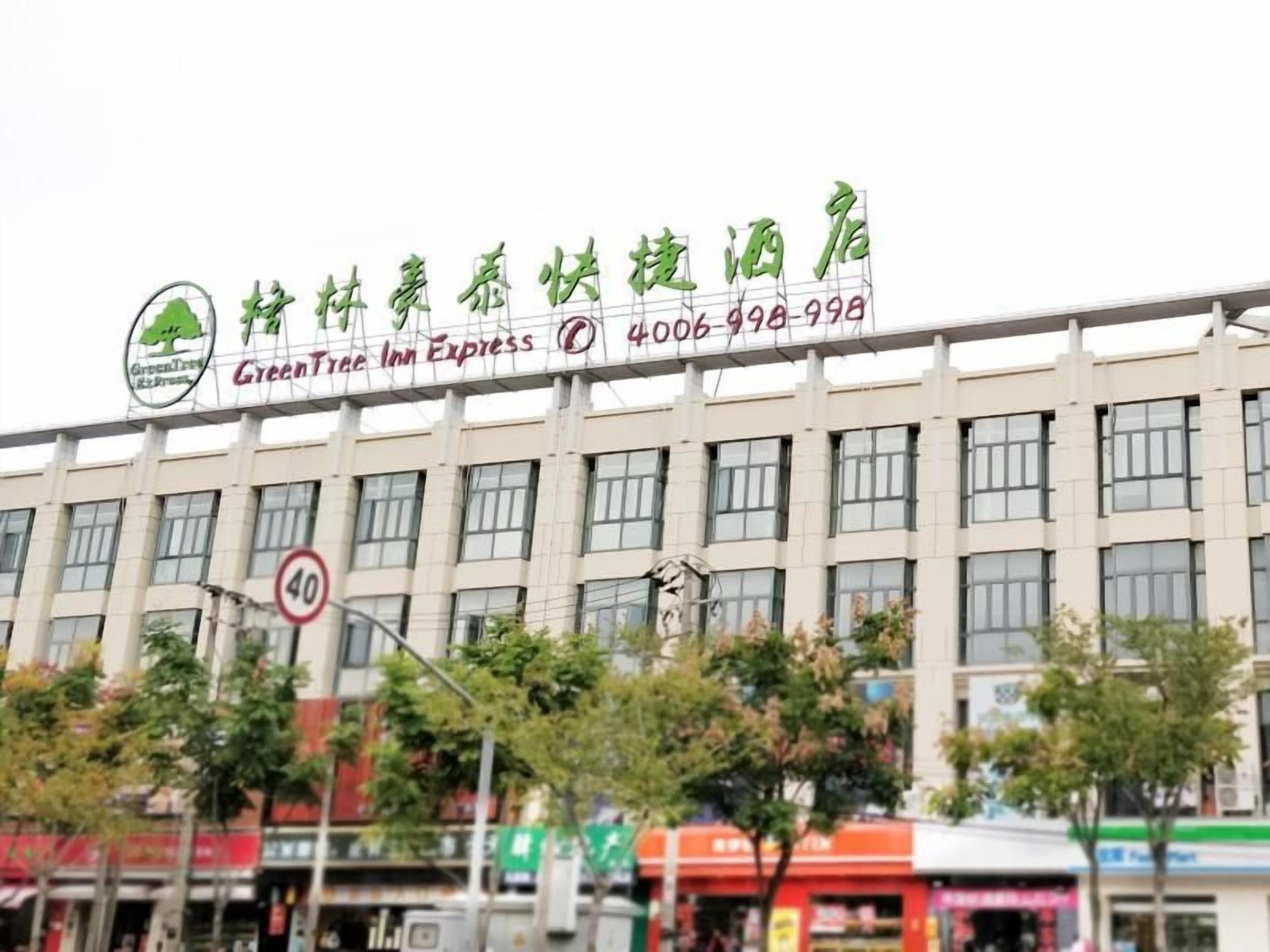 A building with a sign for GreenTree Inn Express, featuring a logo with a tree and the name in English and Chinese.