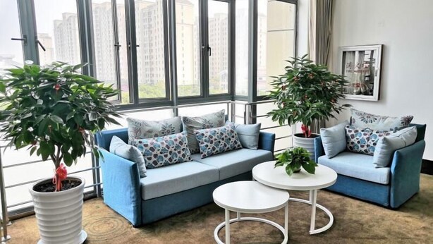 A modern living room with a blue sofa set, two white coffee tables, and large potted plants. - Greentree Inn Shanghai Jinshan District Wanda Plaza Longhao Road Express Hotel (Shanghai)
