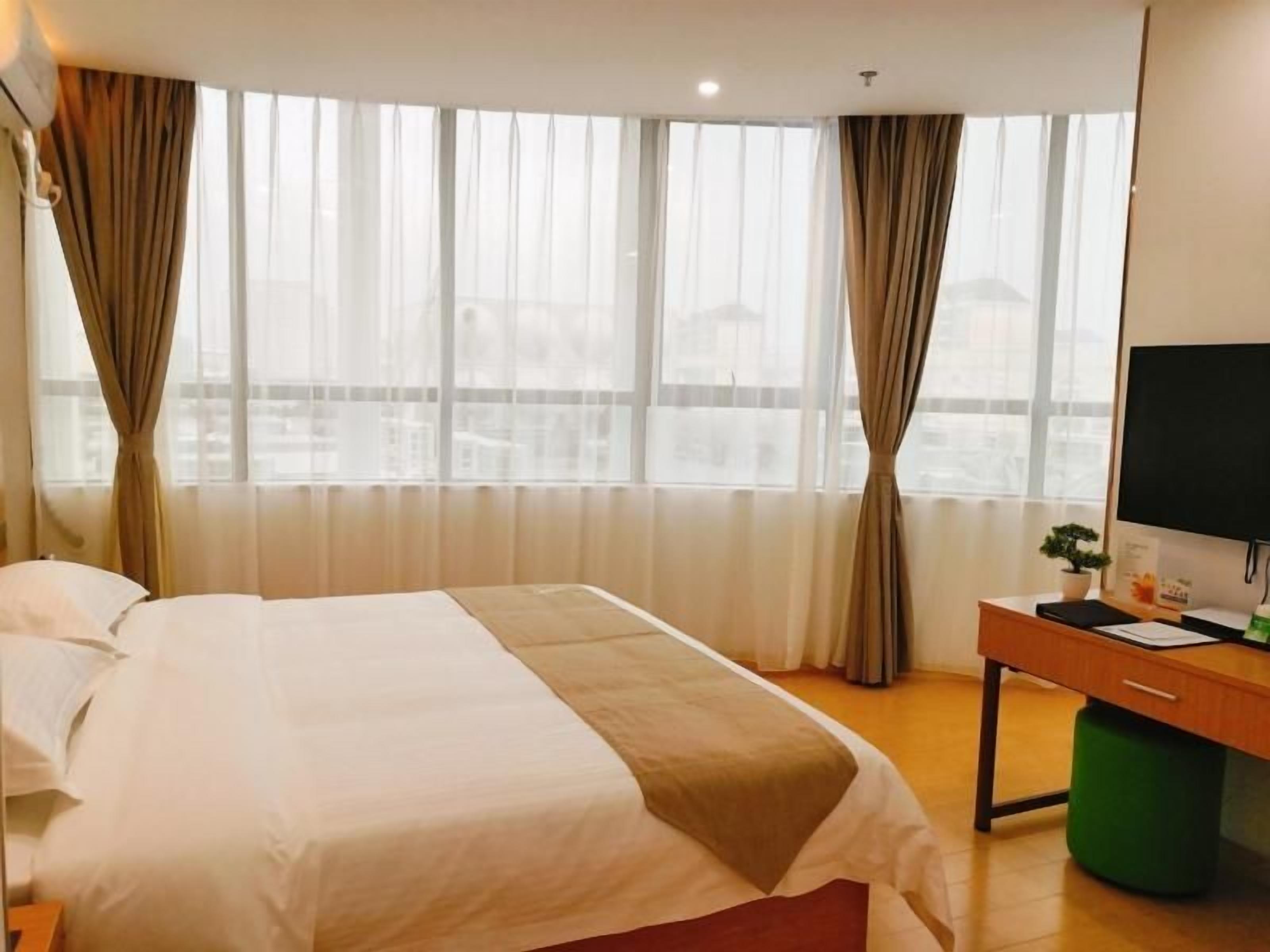 A hotel room with a bed, a desk, a television, and a window with curtains.