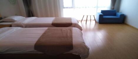 A hotel room with two beds, a blue sofa, and a large window.