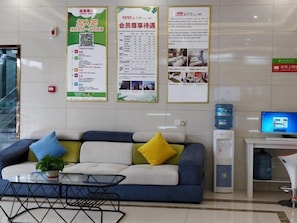 Un espace d’accueil avec un canapé, une table basse et un bureau avec un ordinateur. Des affiches d’information sont accrochées au mur.