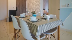 A dining area with a checkered tablecloth, white chairs, and a vase with flowers.