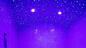 Habitación iluminada en morado, con bañera, paredes de azulejos y techo con luces pequeñas.