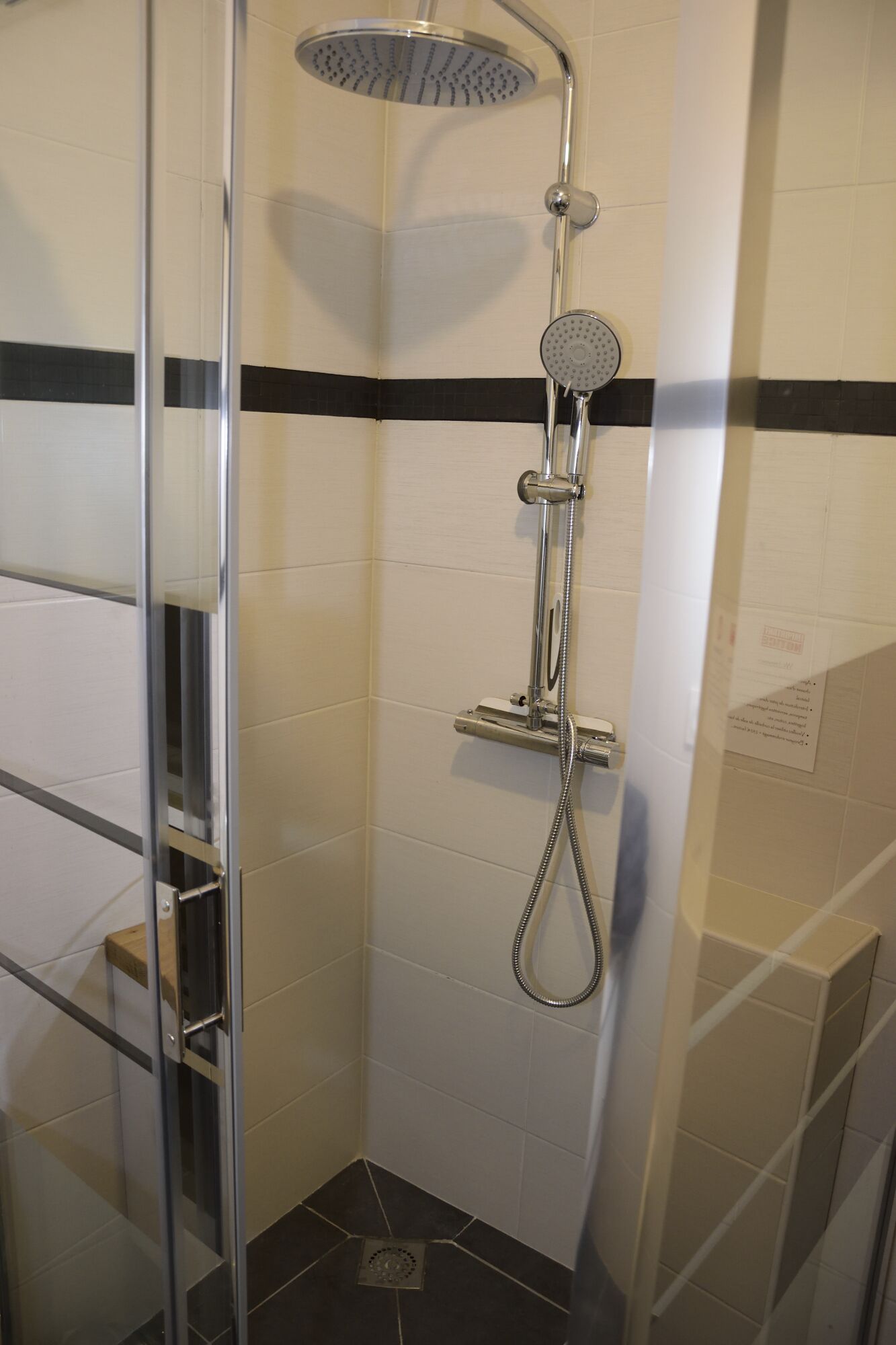 Een douche met een handdouche en een vastgeplaatste douchekop, een glazen deur en een betegelde vloer.