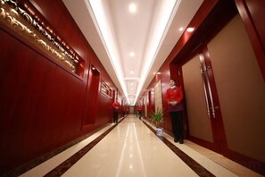Un pasillo de hotel con piso pulido, paredes rojas y una persona con uniforme de pie cerca de una puerta.