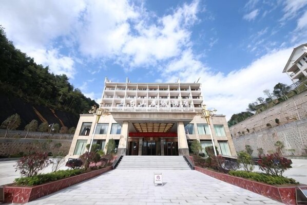 A multi-story building with a central entrance, surrounded by landscaped gardens and a stone wall.