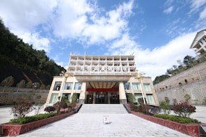 Un edificio de varios pisos con una entrada central, rodeado de jardines ajardinados y un muro de piedra.