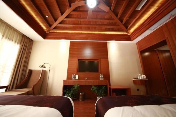 Habitación de hotel con techo de madera, televisor de pantalla plana montado en la pared, dos camas, un escritorio con silla y una mesita de noche con lámpara.