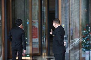 Dos hombres con traje de pie frente a la entrada de un edificio con puertas de cristal.
