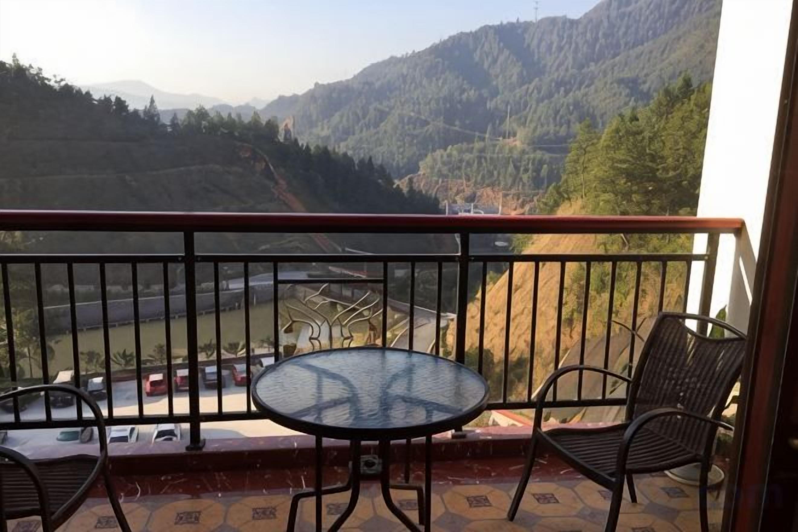 A balcony with a table and chairs, overlooking a valley with mountains.