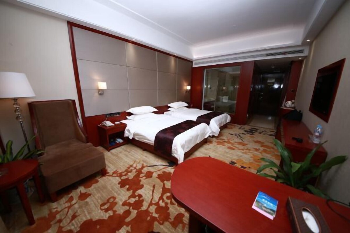 Una habitación de hotel con cama, escritorio, silla, lámpara y televisión.
