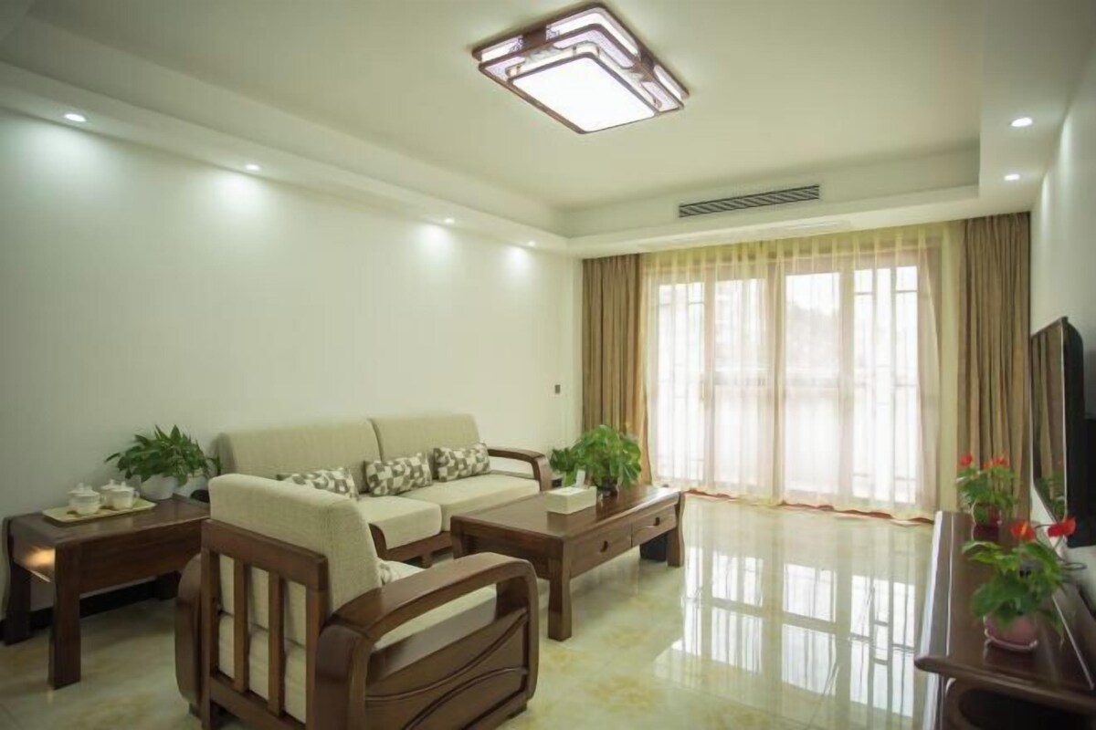 Una sala de estar moderna con sofá, mesa de centro y mueble para la televisión, con un amplio ventanal con cortinas.