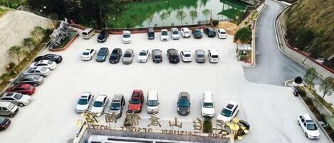 A parking lot with multiple rows of cars, a swimming pool, and a building with a sloped roof.