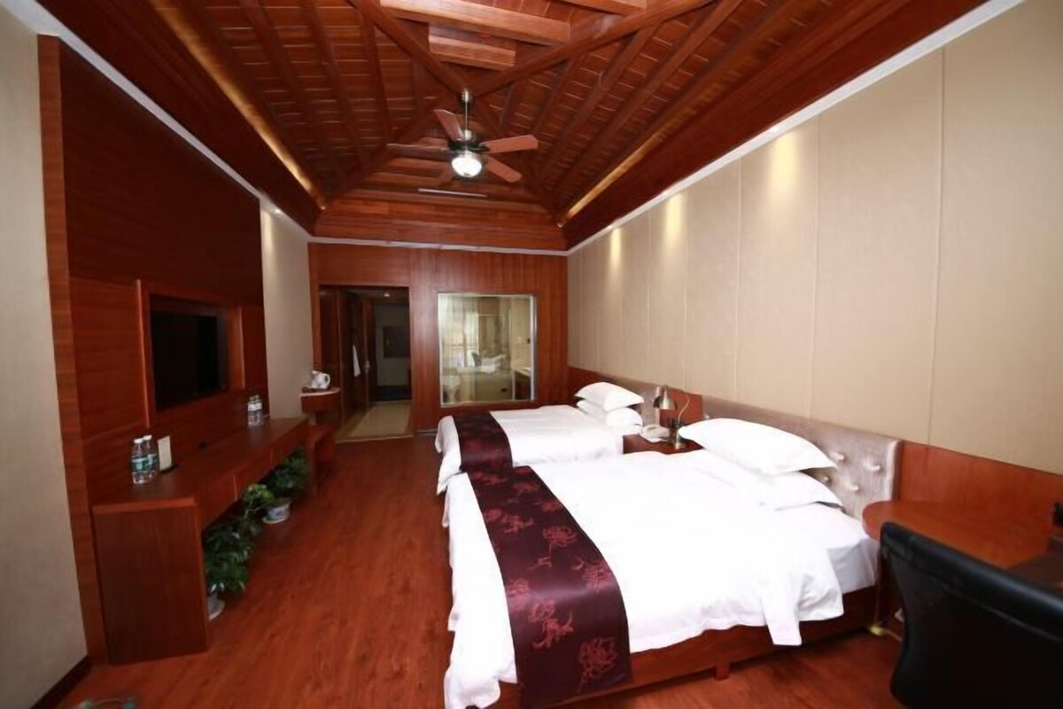 Habitación de hotel con techo de madera, cama con ropa blanca, televisor sobre una consola de madera y un pequeño rincón de descanso.