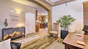 A modern living room with a wooden dining table, a leather sofa, and a decorative console. A large potted plant and a wall-mounted light fixture are also visible. - Family Gem in Phoenix w/ Saltwater Pool & Theater (Gilbert)