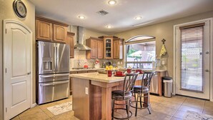 A kitchen with wooden cabinets, stainless steel appliances, and a large island with bar stools. - Family Gem in Phoenix w/ Saltwater Pool & Theater (Gilbert)