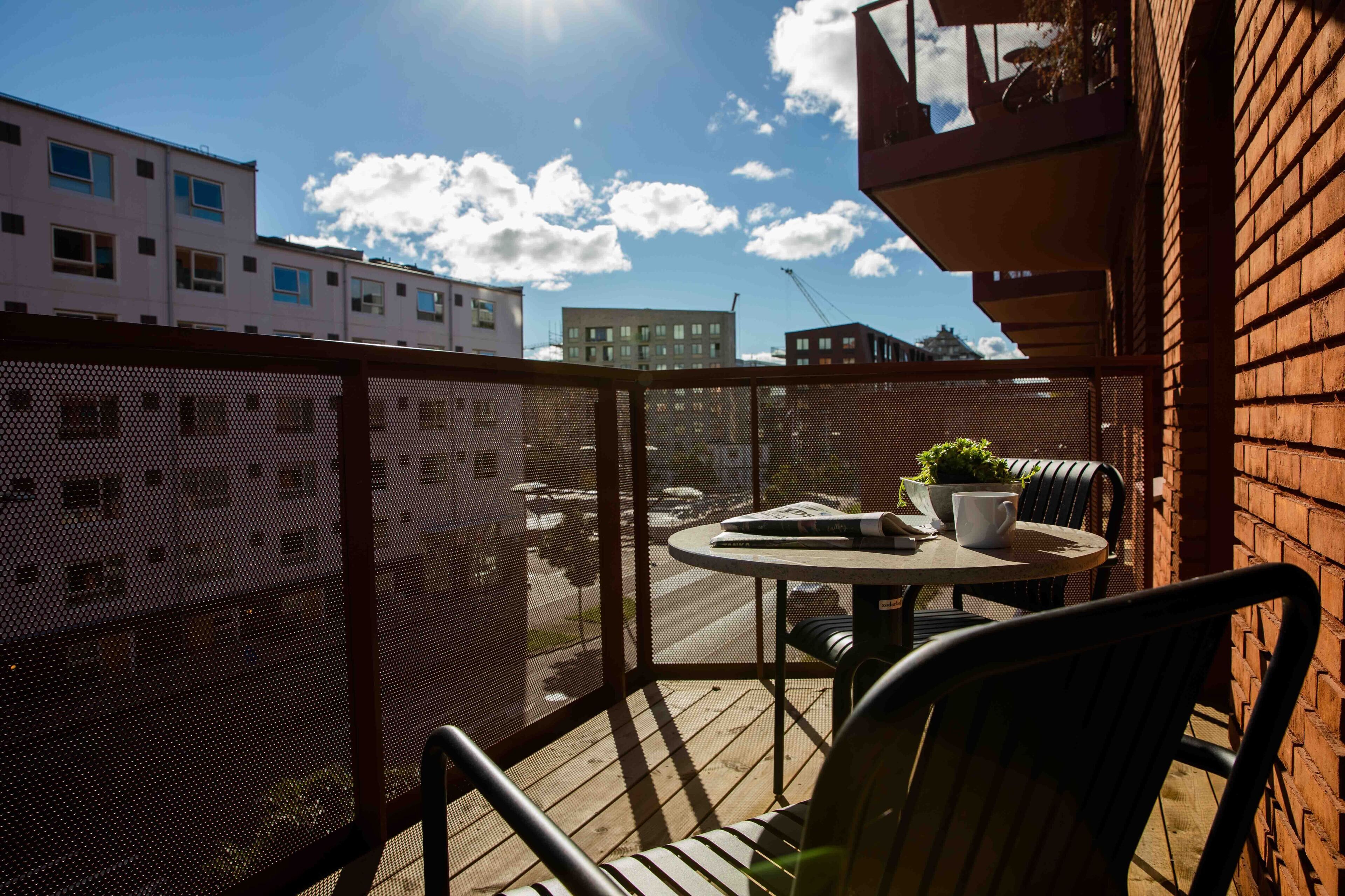 A balcony with a round table and chairs, a potted plant, and a view of buildings in the background.
