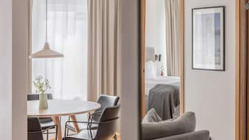 A modern hotel room with a dining area, a bed with a gray bedspread, and a framed picture on the wall.
