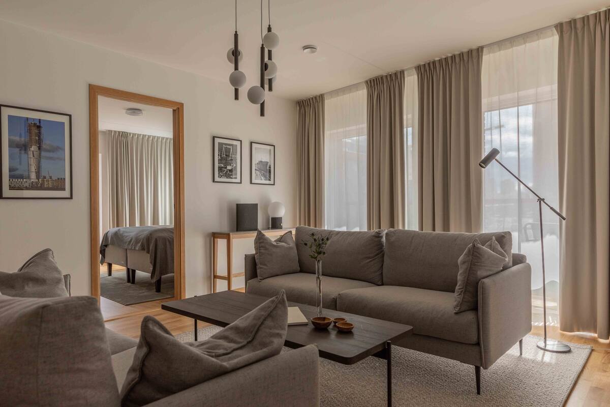 Een moderne woonkamer met een bank, salontafel en een spiegel die de kamer weerspiegelt.