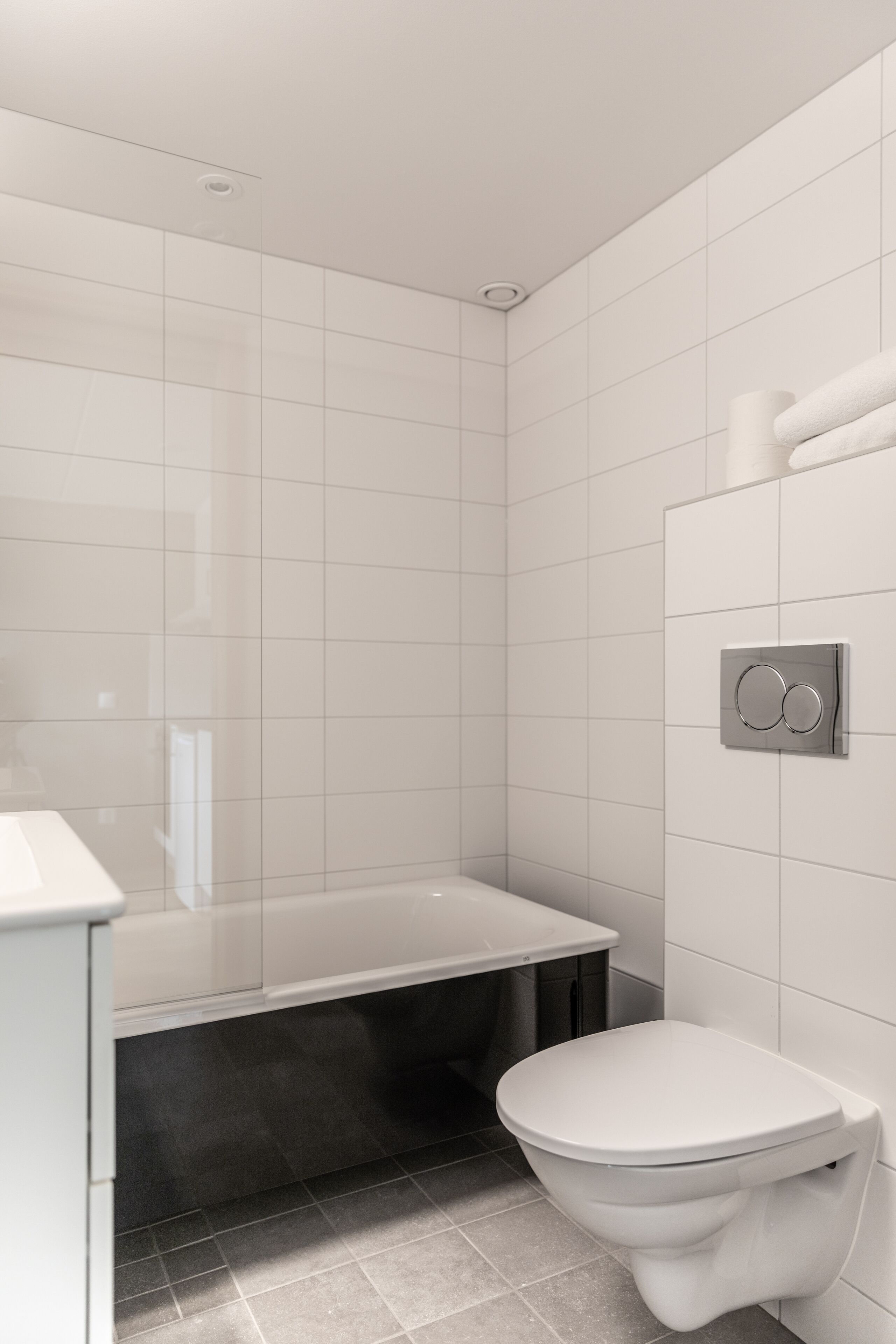 Een moderne badkamer met een bad, toilet en een wandbevestigde zeepdispenser.