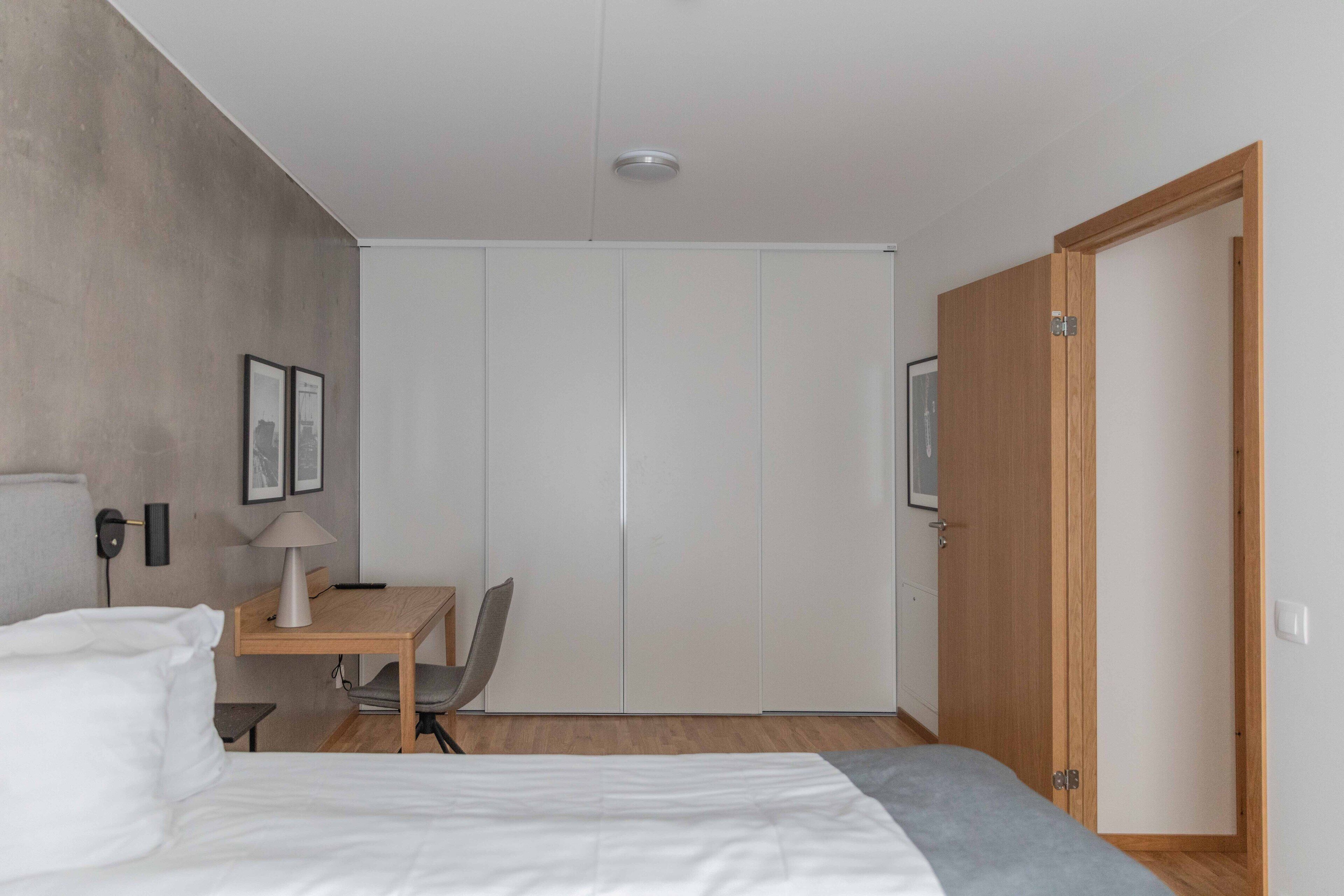 Ein Schlafzimmer mit Bett, Schreibtisch, Stuhl, Kleiderschrank und einer Tür.