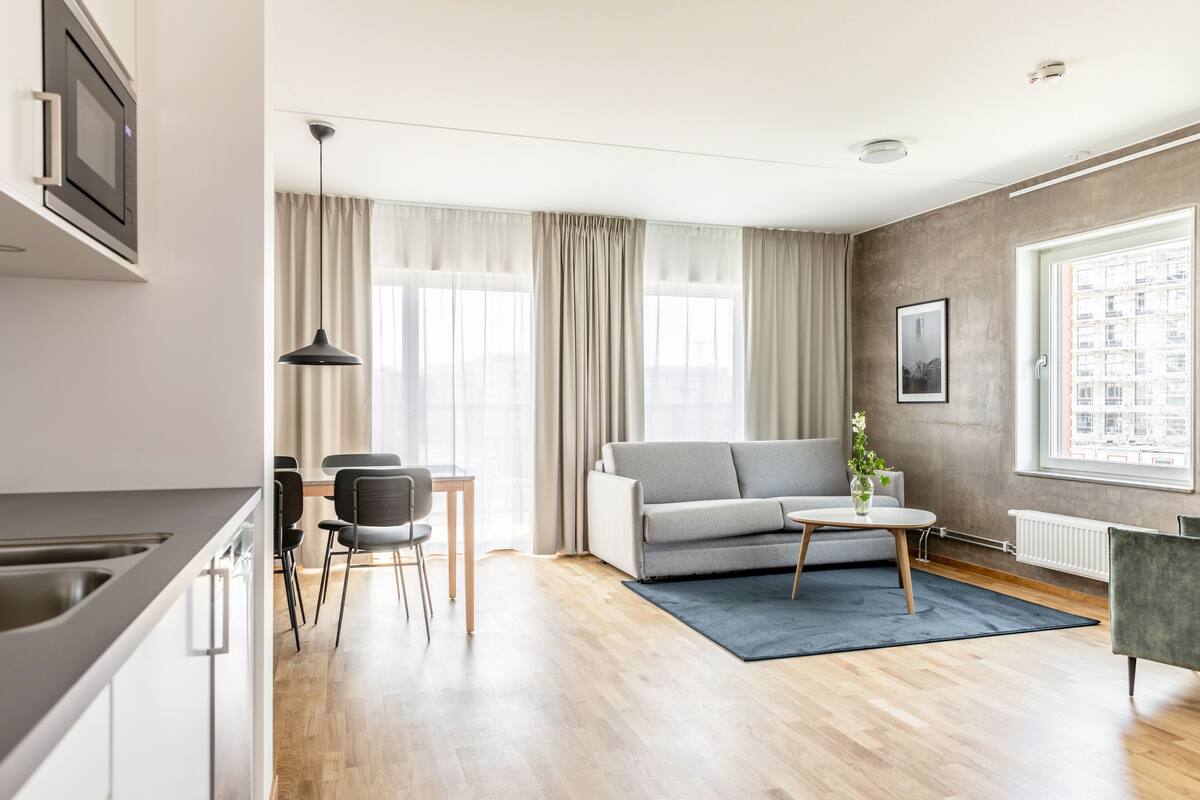 Een moderne woonkamer met een grijze bank, een klein rond tafeltje en een eethoek met stoelen.