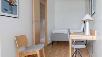 Een kleine, netjes ingerichte kamer met een houten bureau, een stoel, een bed en een lamp.