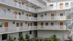 Een meerlaags woongebouw met balkons, een binnentuin met bomen en een heldere lucht.